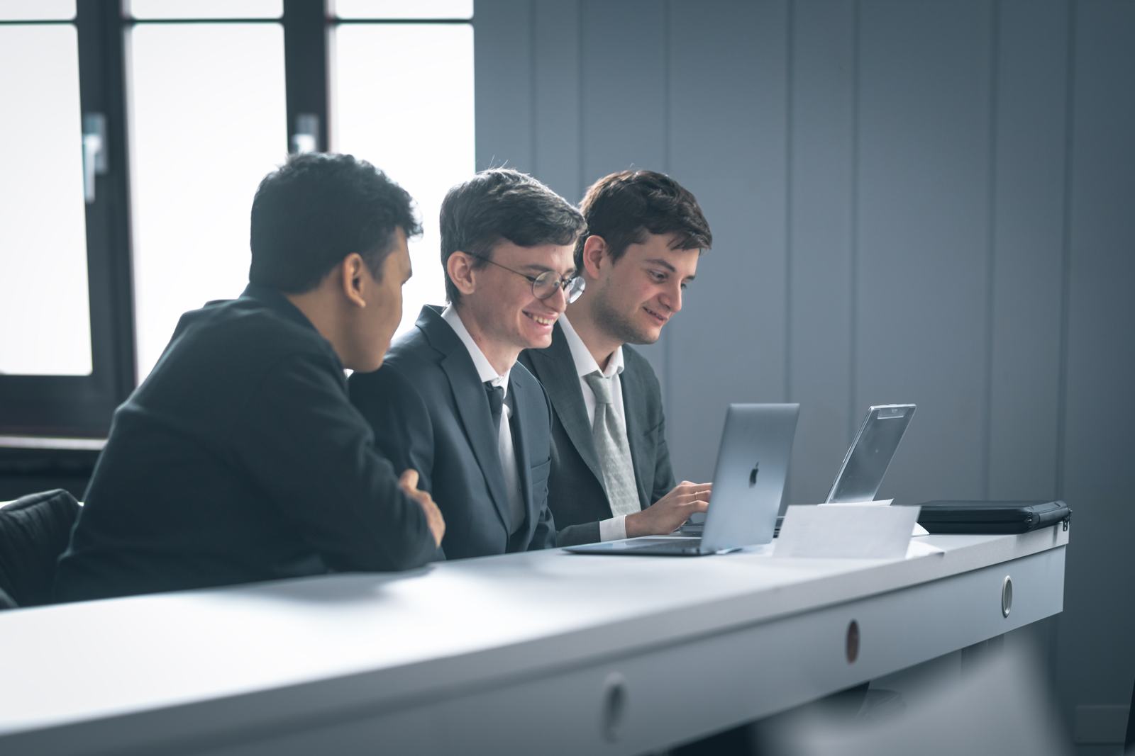 Three BHMS students in business dress working together on laptops