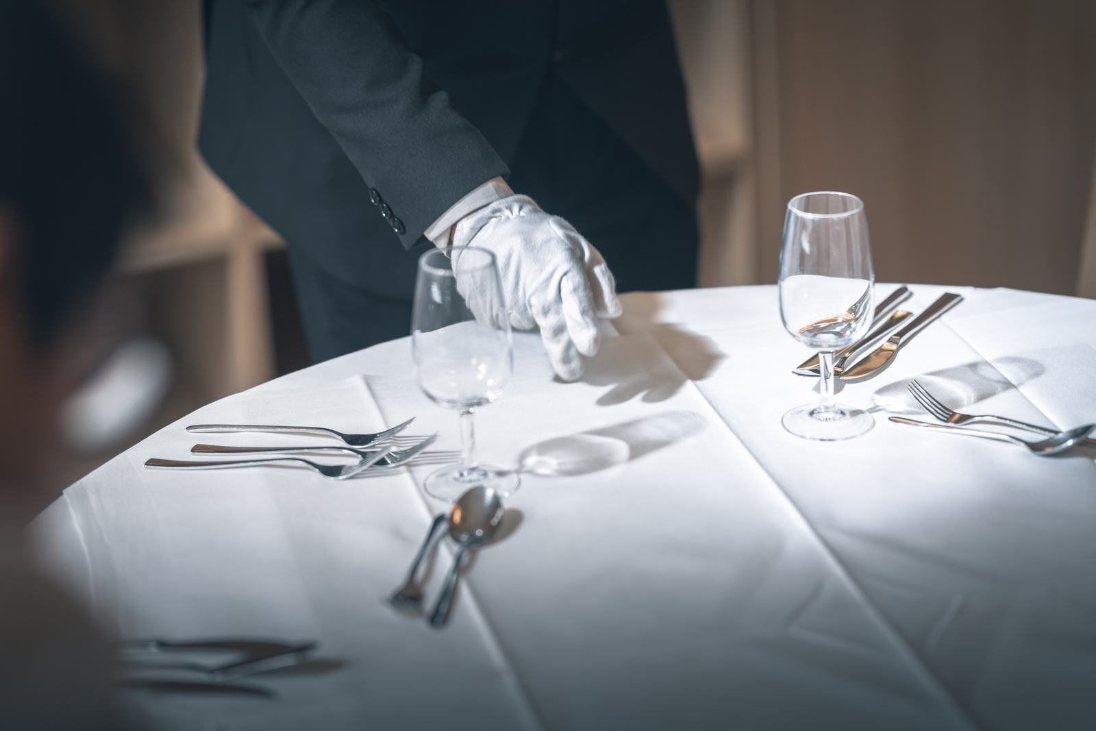 A white-gloved BHMS student laying fine-dining table settings during service training